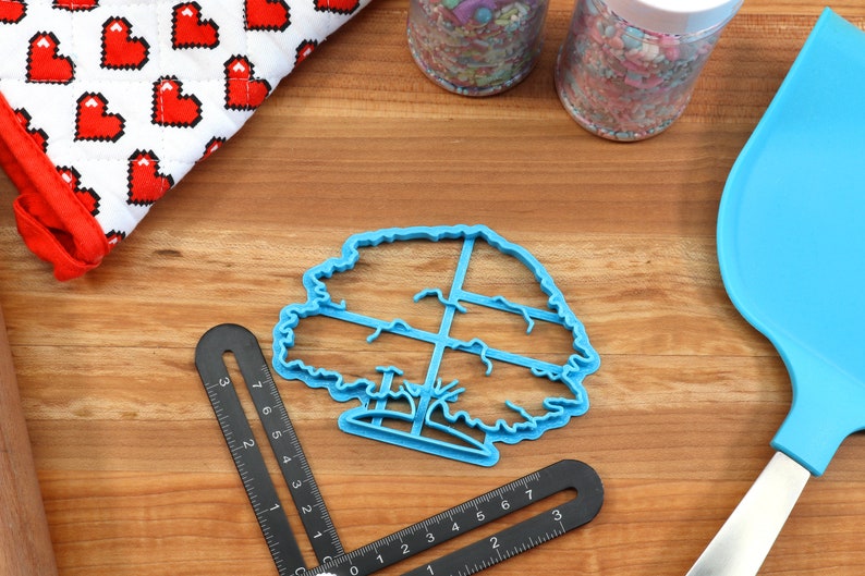 Puede incluir: Cortador de galletas de pl&aacute;stico azul en forma de &aacute;rbol con un contorno detallado. El cortador tiene un patr&oacute;n de cuadr&iacute;cula dentro de la forma del &aacute;rbol.