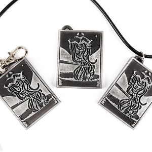 May include: Three silver-toned pendants with black and white images of a creature with tentacles. The pendants are on a white background. One pendant is on a black cord, and another is on a silver key chain.