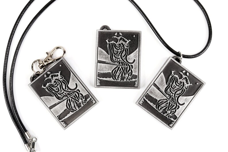 May include: Three silver-toned pendants with black and white images of a creature with tentacles. The pendants are on a white background. One pendant is on a black cord, and another is on a silver key chain.
