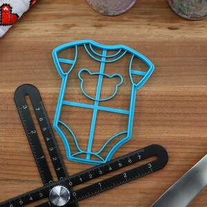May include: A blue plastic cookie cutter shaped like a baby onesie with a bear face on the front.