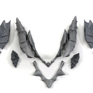 May include: A set of nine grey plastic pieces that can be assembled to create a dragon's wings. The pieces are detailed with a textured, scaly design.