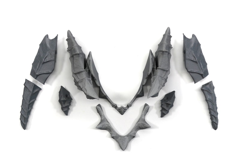 May include: A set of nine grey plastic pieces that can be assembled to create a dragon's wings. The pieces are detailed with a textured, scaly design.