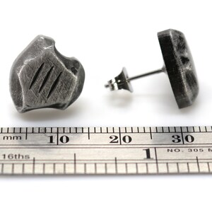 May include: A pair of silver stud earrings with a textured, irregular shape. The earrings are approximately 1 cm in diameter.