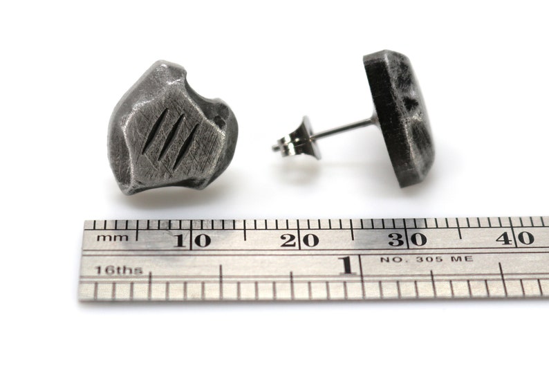 May include: A pair of silver stud earrings with a textured, irregular shape. The earrings are approximately 1 cm in diameter.