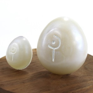 May include: Two white eggs with a swirl design on a wooden surface. The eggs are different sizes.