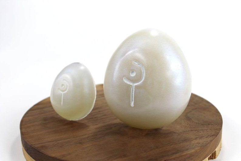 May include: Two white eggs with a swirl design on a wooden surface. The eggs are different sizes.