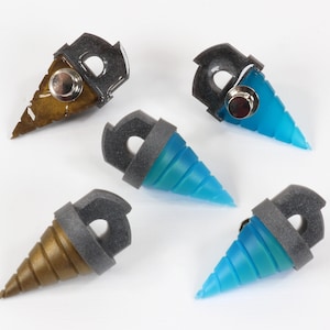 May include: Five drill-shaped objects with a metallic gray top and a button. The drill bits are in shades of brown and blue. The objects are arranged on a white surface.
