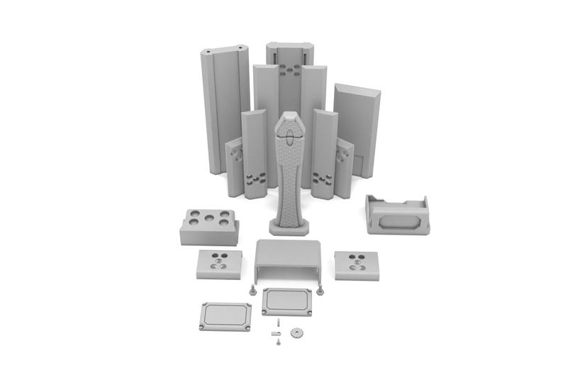 K&ouml;nnte beinhalten: Eine Sammlung grauer, 3D-gedruckter Komponenten, darunter rechteckige Bl&ouml;cke, ein hohes, strukturiertes Mittelst&uuml;ck und verschiedene Kleinteile. Die Teile sind auf wei&szlig;em Hintergrund angeordnet, was auf ein Kit oder eine Reihe modularer Elemente hindeutet.