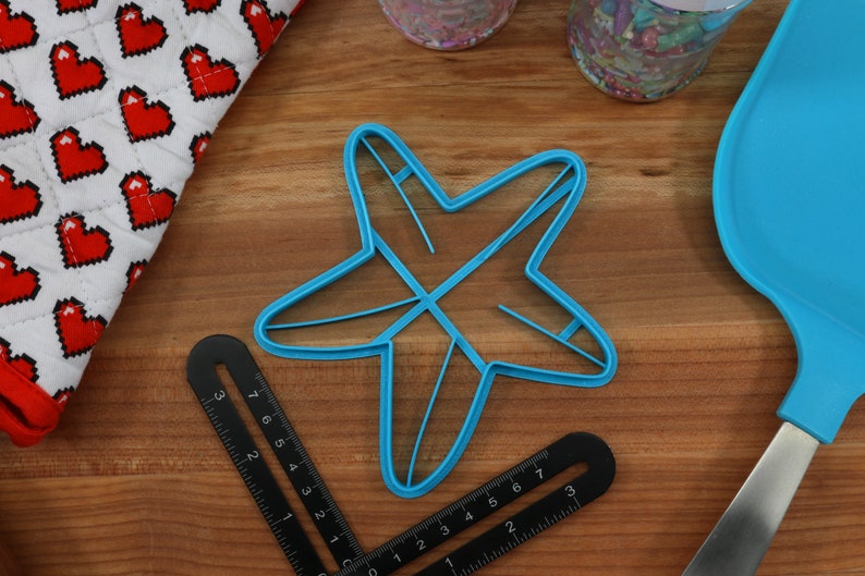 May include: A blue plastic star-shaped cookie cutter on a wooden surface.