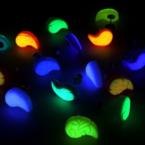 May include: A set of 12 glow-in-the-dark earrings in various colors and shapes. The earrings are made of polymer clay and have a stud back.