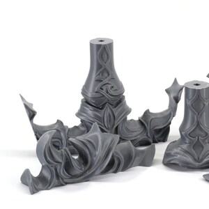 May include: Five gray 3D printed plastic pieces with intricate, detailed designs. The pieces are likely parts of a larger model or sculpture.