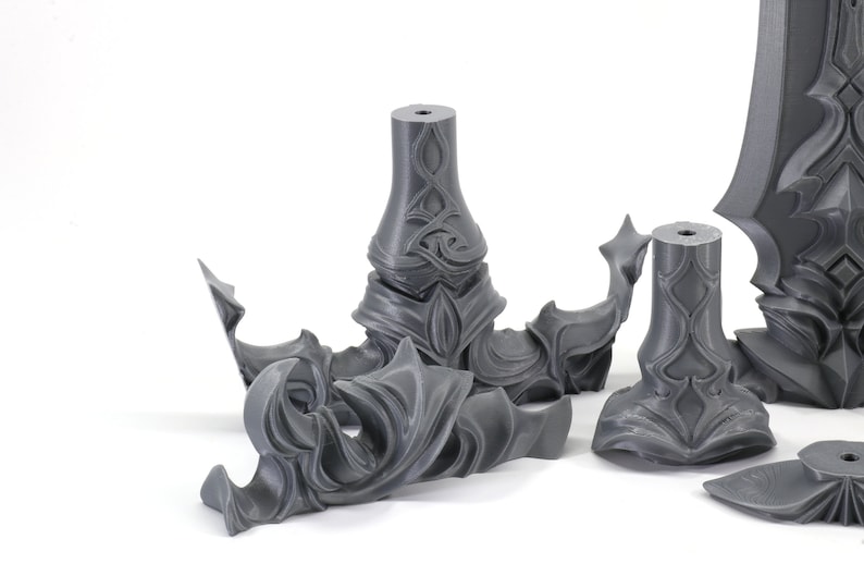 May include: Five gray 3D printed plastic pieces with intricate, detailed designs. The pieces are likely parts of a larger model or sculpture.