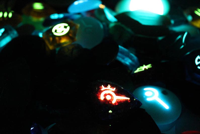 Puede incluir: Primer plano de una colecci&oacute;n de accesorios de juego brillantes, que incluyen un mando rojo y negro con un s&iacute;mbolo, un mando azul y blanco con un s&iacute;mbolo y un mando verde y negro con un s&iacute;mbolo.