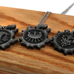 May include: Three silver necklaces with pendants featuring different designs. The pendants are circular and have a gear-like edge. The designs include a scale, a ship, and a flower.