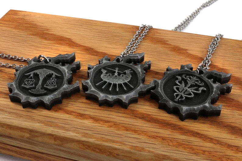 May include: Three silver necklaces with pendants featuring different designs. The pendants are circular and have a gear-like edge. The designs include a scale, a ship, and a flower.