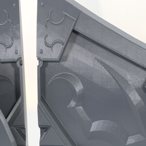May include: Two gray, 3D printed, interlocking pieces of a puzzle. The pieces have a geometric design with a raised, textured surface.