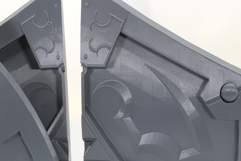 May include: Two gray, 3D printed, interlocking pieces of a puzzle. The pieces have a geometric design with a raised, textured surface.