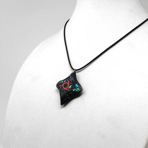 Pu&ograve; includere: Una collana nera con un ciondolo nero e verde con un design a spirale rosso. Il ciondolo ha la forma di un diamante.