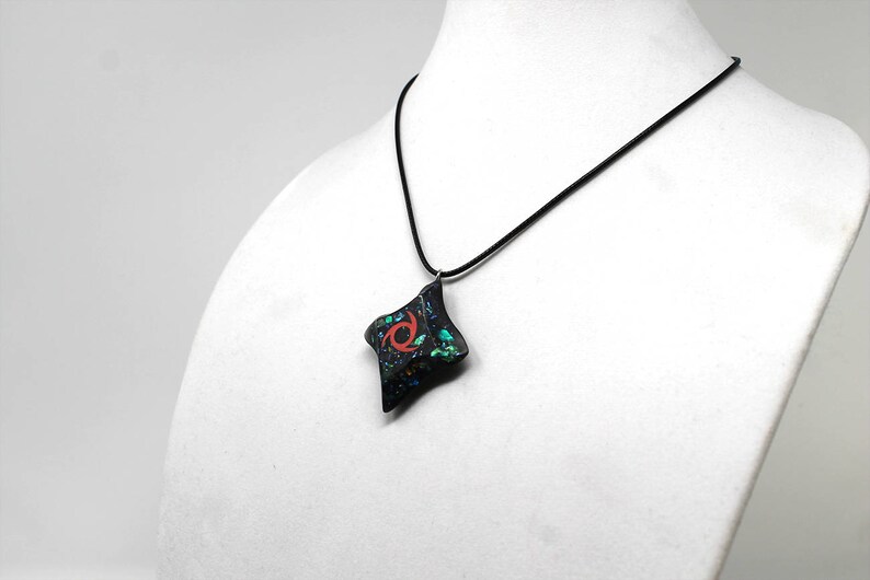 Pu&ograve; includere: Una collana nera con un ciondolo nero e verde con un design a spirale rosso. Il ciondolo ha la forma di un diamante.