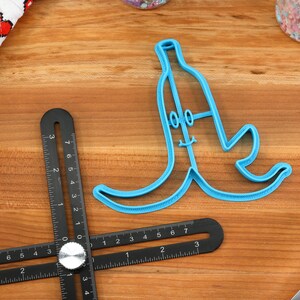 May include: A blue plastic banana-shaped cookie cutter with a smiling face and two eyes. The cutter is on a wooden surface.