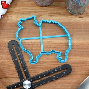 May include: A blue plastic cookie cutter shaped like a Pomeranian dog. The cutter is on a wooden surface with a ruler and other baking tools.