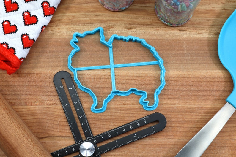 May include: A blue plastic cookie cutter shaped like a Pomeranian dog. The cutter is on a wooden surface with a ruler and other baking tools.