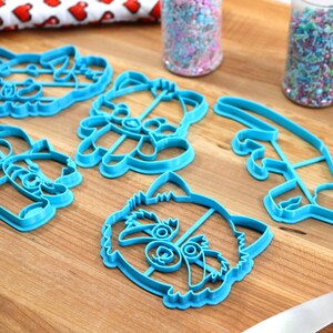 May include: Set of six blue plastic cookie cutters shaped like a raccoon, including a full face, a head, a tail, and two different poses of the raccoon holding a stick.