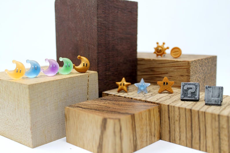May include: A set of colorful and metallic earrings featuring various video game characters and items, including a gold coin, a star, a question block, and a crescent moon.