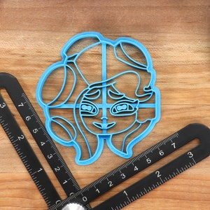 May include: A blue plastic cookie cutter shaped like a cartoon character with long hair and large eyes.