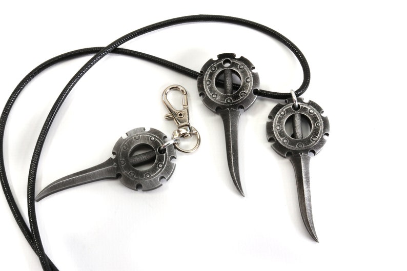 May include: Three silver-colored metal pendants with a circular design and a pointed tip. The pendants are attached to a black cord.