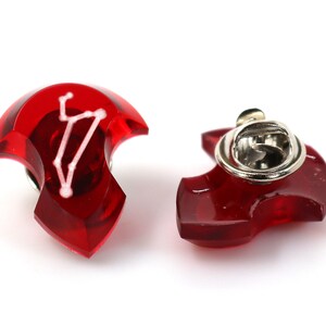 May include: Red enamel pin with a white constellation design. The pin has a silver metal clasp on the back.