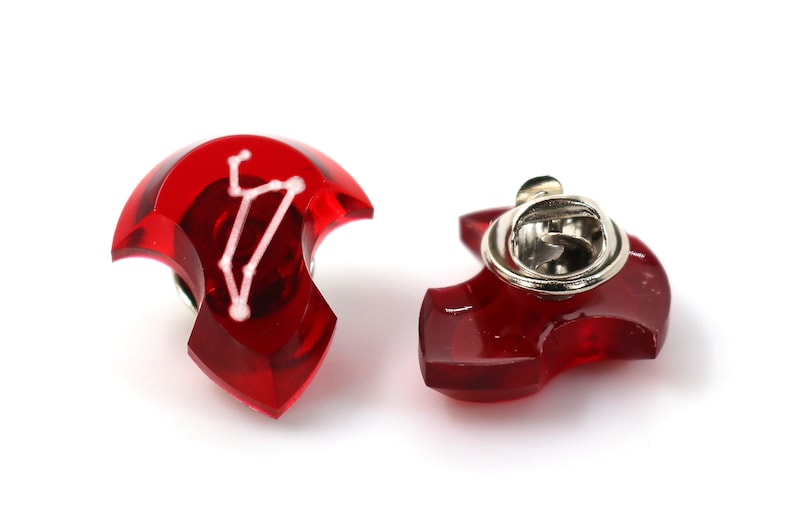 May include: Red enamel pin with a white constellation design. The pin has a silver metal clasp on the back.