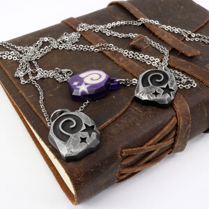 May include: Three silver necklaces with pendants featuring a spiral design and stars. The pendants are on a brown leather journal.