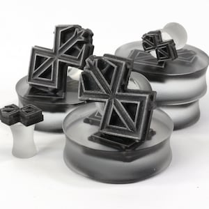 May include: Four black geometric shaped plugs for stretched earlobes, displayed on clear glass bases. The plugs are in various sizes and shapes.