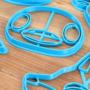 May include: A set of four blue plastic cookie cutters shaped like animal faces. The cutters are on a wooden surface.