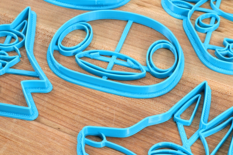 May include: A set of four blue plastic cookie cutters shaped like animal faces. The cutters are on a wooden surface.