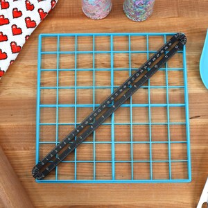 May include: A blue baking sheet with a grid pattern, a black ruler, a wooden rolling pin, a blue spatula, and a red and white oven mitt.