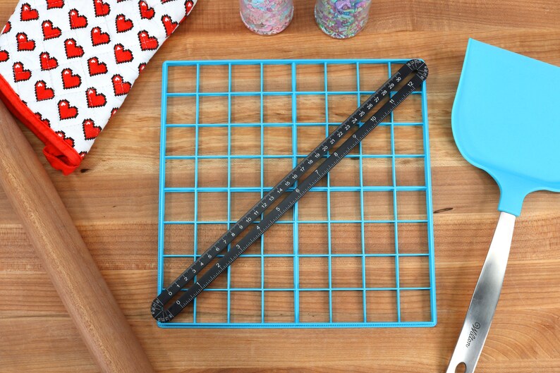 May include: A blue baking sheet with a grid pattern, a black ruler, a wooden rolling pin, a blue spatula, and a red and white oven mitt.
