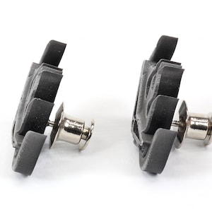 May include: Two black plastic snap fasteners with silver metal posts. The fasteners are designed to be used for attaching fabric or other materials together.