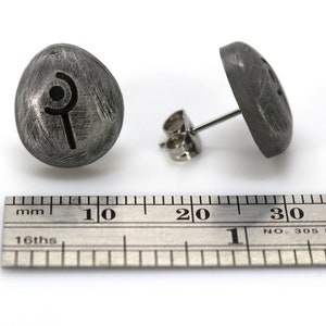 May include: A pair of silver stud earrings with a stylized symbol on the front. The earrings are approximately 1 cm in diameter.