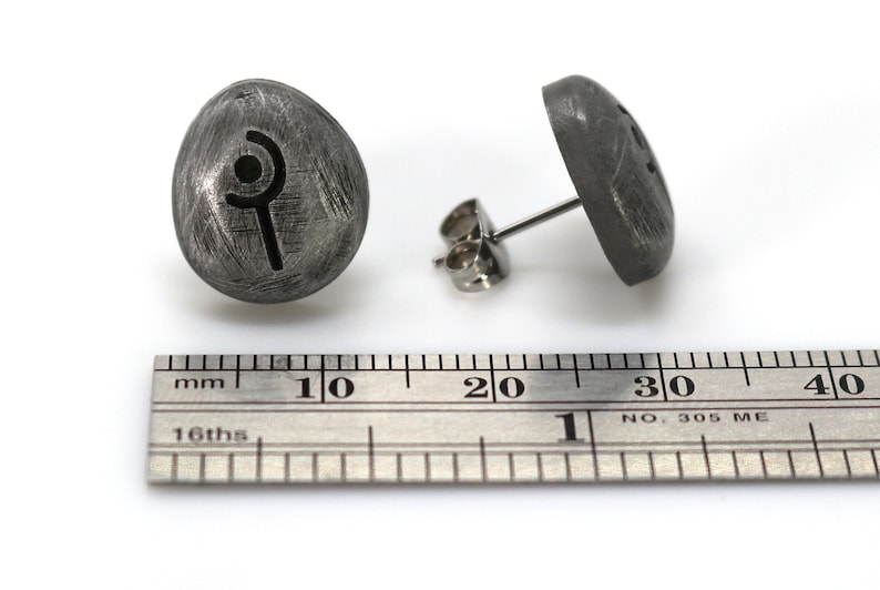 May include: A pair of silver stud earrings with a stylized symbol on the front. The earrings are approximately 1 cm in diameter.