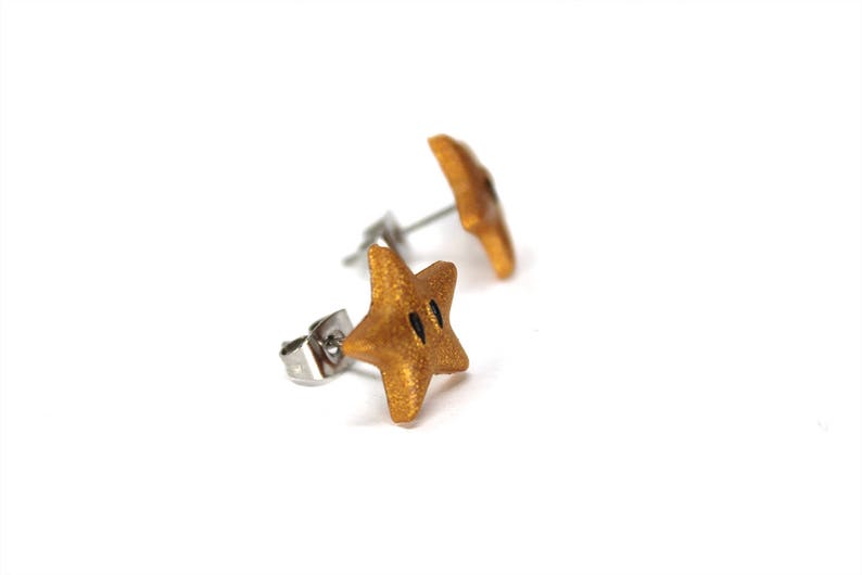 May include: A pair of gold star-shaped earrings with black accents. The earrings are made of polymer clay and have a shiny finish.