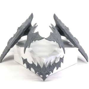May include: Three grey 3D printed bat-shaped objects. Two are larger and have a more detailed design, while the third is smaller and simpler.