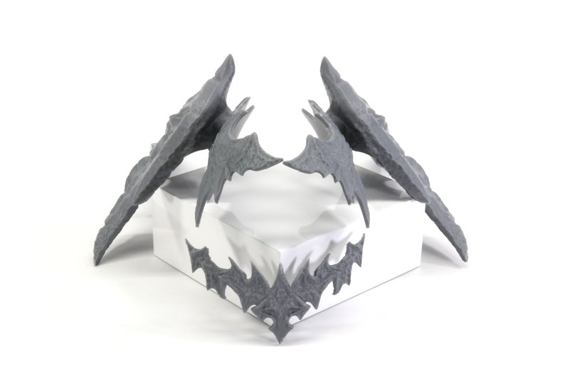 May include: Three grey 3D printed bat-shaped objects. Two are larger and have a more detailed design, while the third is smaller and simpler.