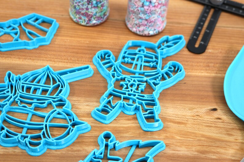 May include: Four blue plastic cookie cutters on a wooden surface. The cutters are shaped like a knight, a hot air balloon, a castle, and a ship.
