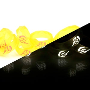 May include: A group of yellow silicone rings with a red design. The rings are stacked on top of each other and are glowing in the dark.