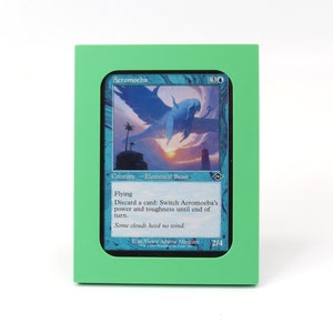 Op de afbeelding: Een groene kaarthouder met een blauwe en witte Magic: The Gathering kaart erin. De kaart toont een blauw wezen met vleugels en de tekst "Aeromoeba".
