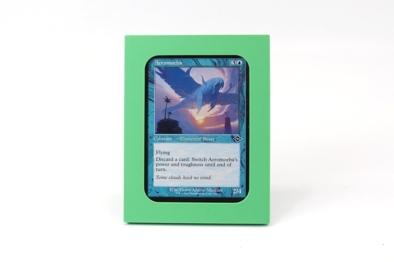 Op de afbeelding: Een groene kaarthouder met een blauwe en witte Magic: The Gathering kaart erin. De kaart toont een blauw wezen met vleugels en de tekst "Aeromoeba".