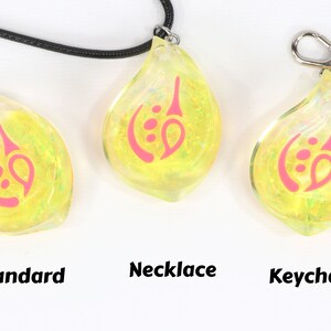 May include: Three yellow iridescent glass pendants with a pink design. The pendants are shown in three different styles: standard, necklace, and keychain.