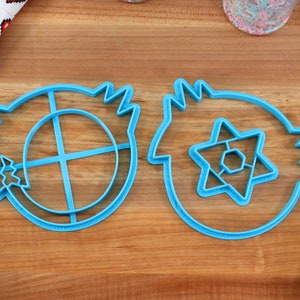 May include: Two blue plastic cookie cutters, one shaped like a circle with a cross inside and the other shaped like a star with a hexagon inside.